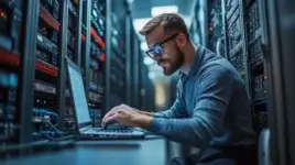 IT professional managing a CMDB on a laptop in a server room, surrounded by network equipment.